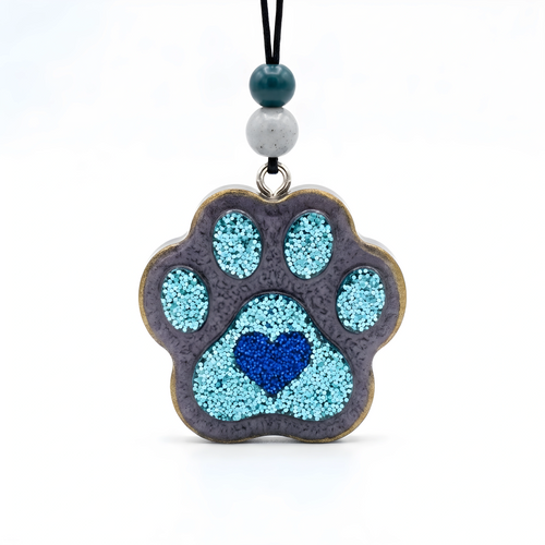 A paw-shaped pendant necklace featuring a textured gray base with light blue glitter accents and a blue heart in the center, hanging from a black cord with two decorative beads on a white background.