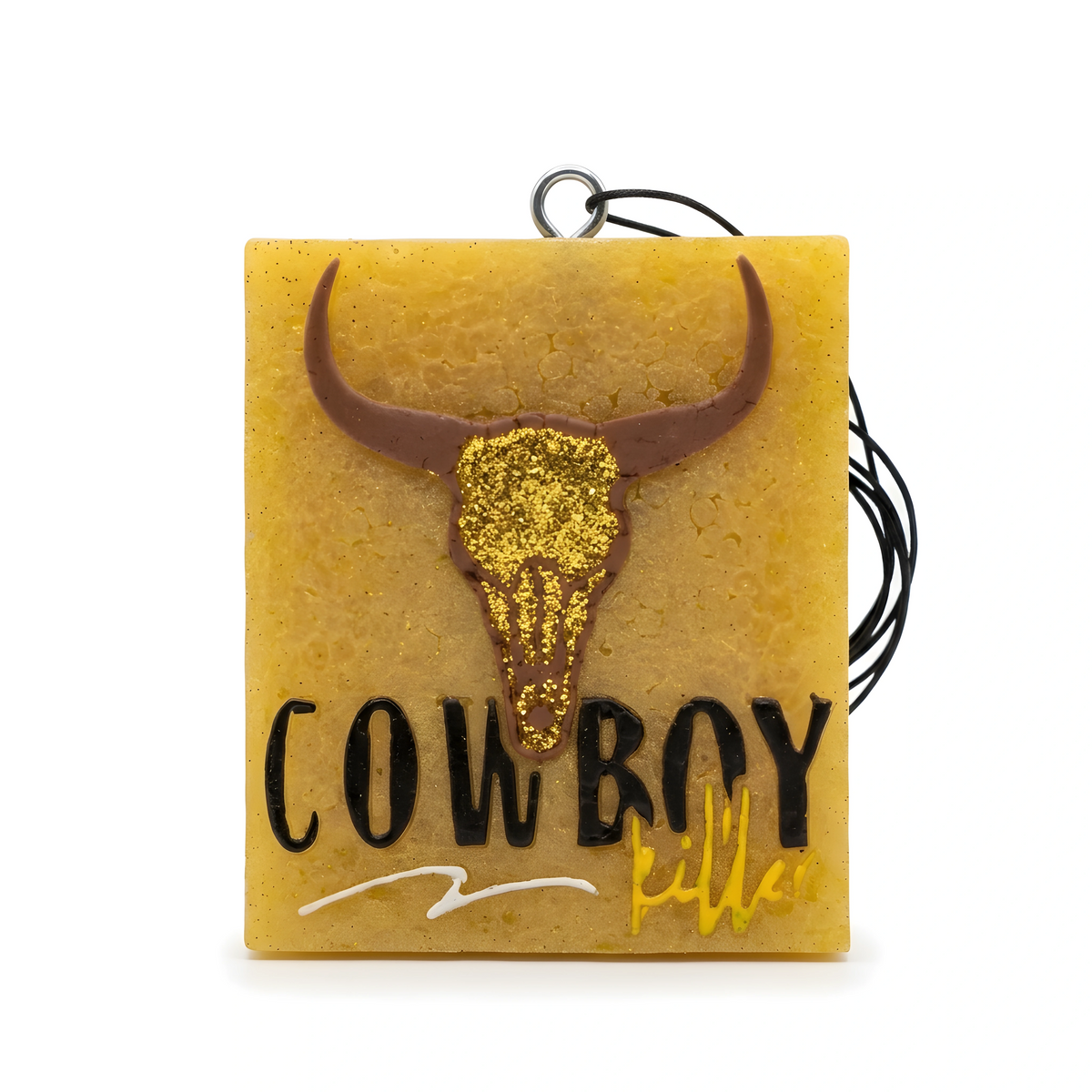 A square amber resin charm with a gold glitter bull skull and the words COWBOY KILLER in black and gold script, hanging from a black cord.