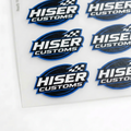 A sheet of die-cut stickers featuring the 'HISER CUSTOMS' logo in blue, white, and black, arranged on a white backing card over a light gray surface.