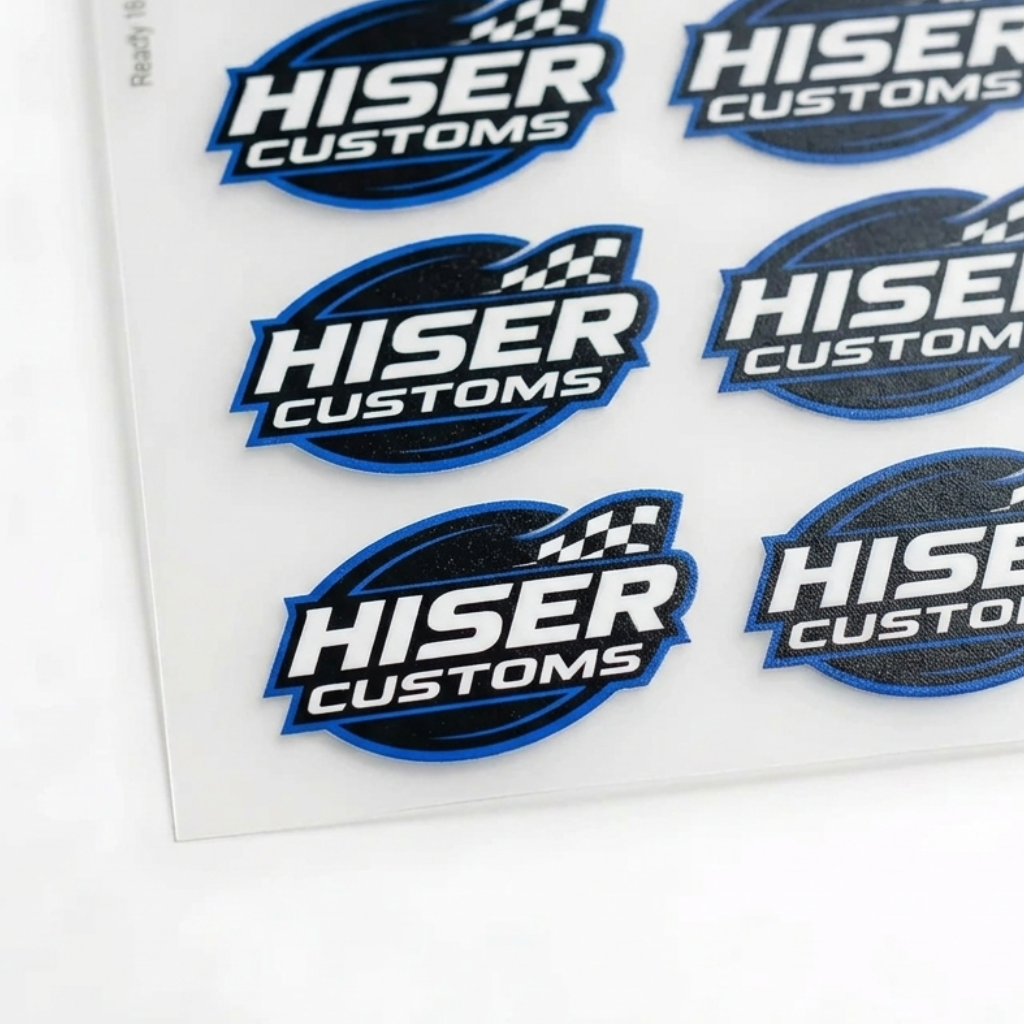 A sheet of die-cut stickers featuring the 'HISER CUSTOMS' logo in blue, white, and black, arranged on a white backing card over a light gray surface.