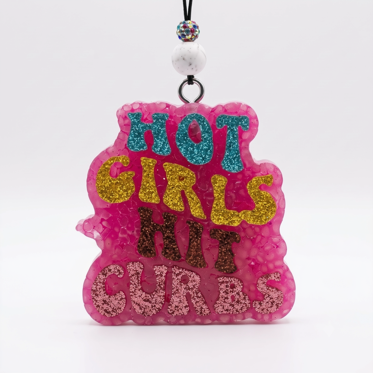 A pink glitter freshie reading "HOT GIRLS HIT CURBS" in teal, gold, and brown glitter lettering, hanging from a beaded cord.