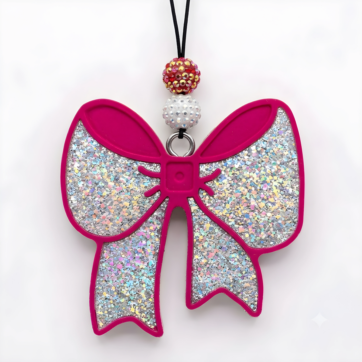 A glittery bow-shaped phone case or charm in iridescent silver glitter with hot pink trim, featuring a black cord and decorative beads at the top, shown on a plain white background.