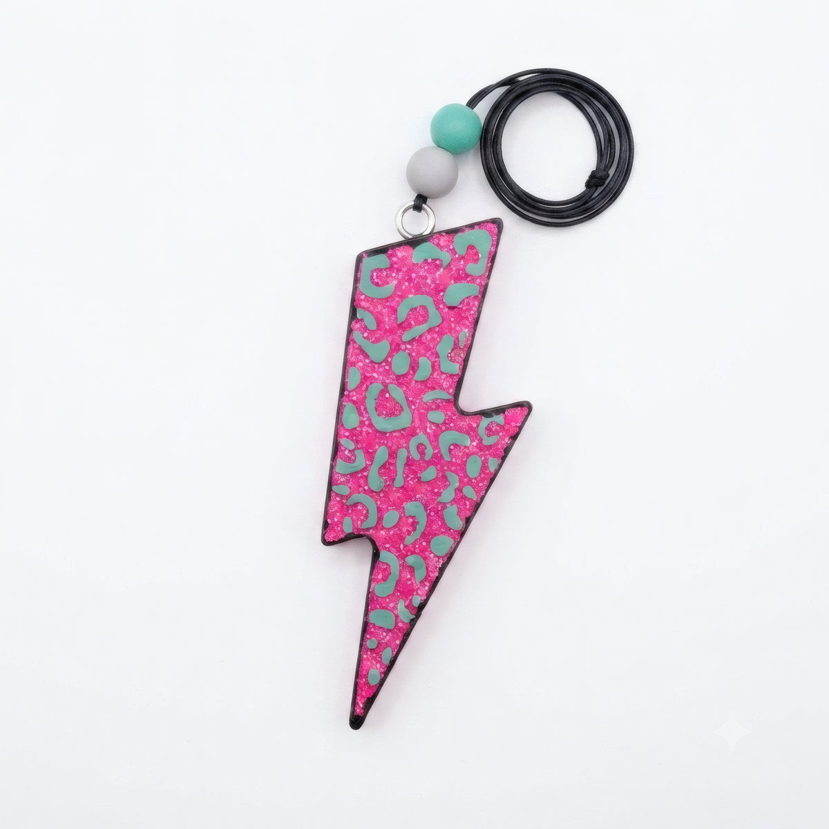 A lightning bolt-shaped pendant with a pink and teal leopard print pattern, attached to a black cord with two decorative beads, shown on a plain white background.