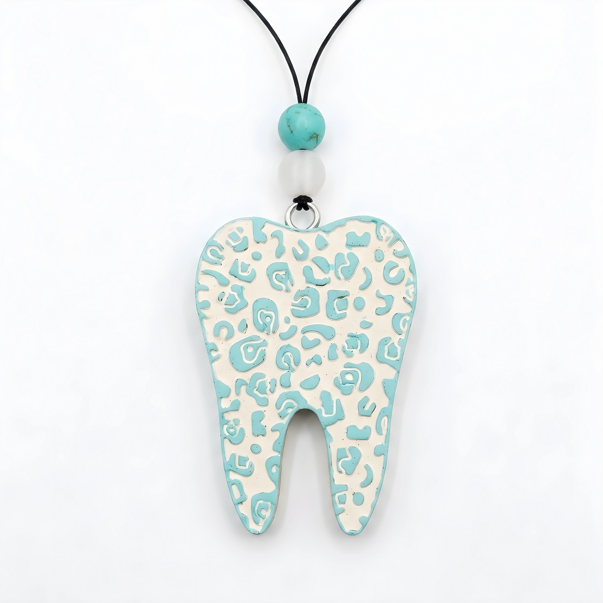 A tooth-shaped pendant necklace with a light blue and off-white leopard print pattern, hanging from a black cord with turquoise and white beads on a white background.