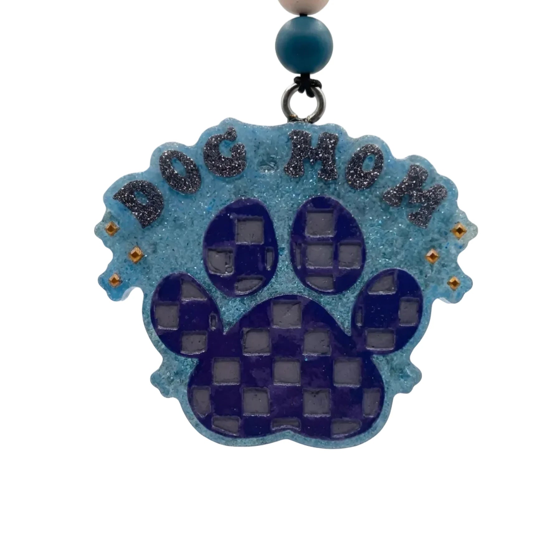 A blue and purple dog paw print ornament with the words 'DOG MOM' in glittery letters, hanging from a beaded string against a light gray background.